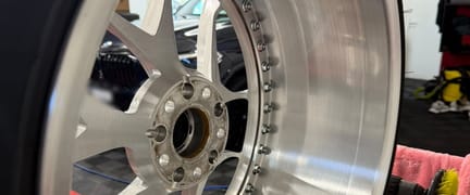 Grossaufnahme einer aufbereiteten mehrteiligen Felge: gebürstetes Aluminium, Verschraubung am Felgenhorn, rechts die Poliermaschine.