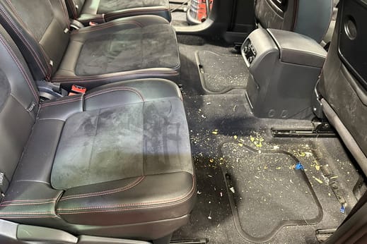 Zweite Sitzreihe desselben Vans vor der Aufbereitung: Schmutz auf dem Boden, Flecken auf der Sitzfläche.