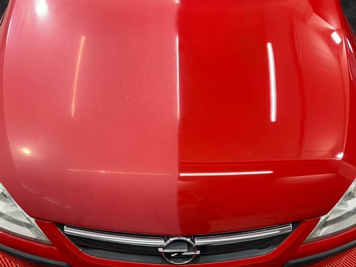 Rote Motorhaube, zur Hälfte poliert: die eine Seite spiegelt das Licht, die andere bleibt matt und stumpf.
