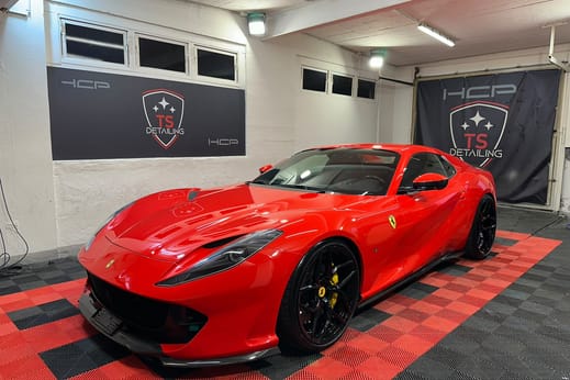 Roter Ferrari im Studio von TS Detailing, dahinter zwei Banner an der Wand.