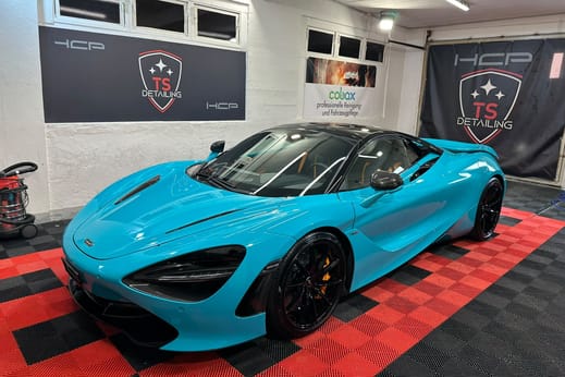 Hellblauer McLaren im Studio von TS Detailing, am Rand die Ausrüstung des Arbeitsplatzes und an der Wand Banner des Betriebs sowie eines Pflegemittel-Herstellers.